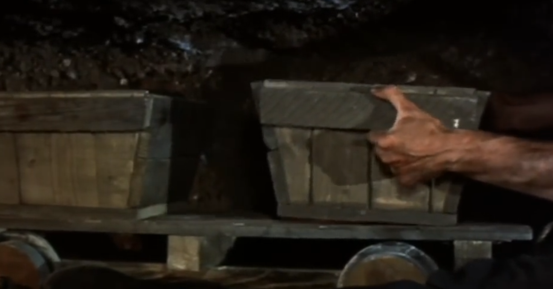 In a tunnel, character lifts a box of dirt onto a trolley.