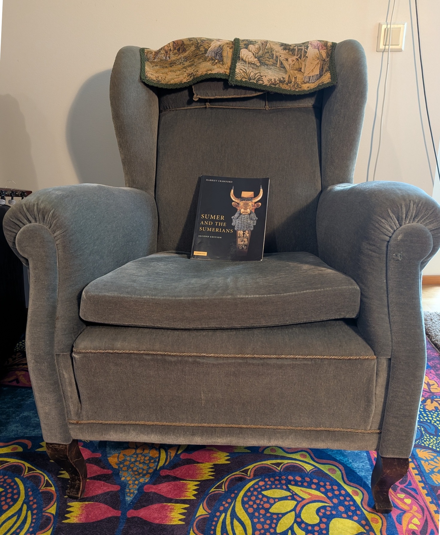 Picture of an armchair in authors home, with a book about Sumerians on it, and loose cables hanging at at the edge of the picture